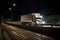 A large american semi-trailer moves along the highway at night with its headlights on