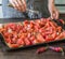 Large baking tray with chopped tomatoes, garlic and onions for making tomato sauce. Chef sprinkles spices or dry herbs of glass