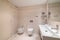 Large bathroom decorated with beige tiles. Square full length mirror and rectangular sink with two faucets, toilet and