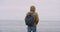 On a large beach man walking to the seashore with a blue bag on the back , amazing view of sea in front of the camera