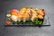 Large beautiful set of different types of sushi maki and nigiri on a black rectangular stone slate plate.