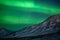 Large belts of green northen light dancing above the peaks of Svalbard mountains