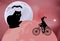 Large black cat sitting on the globe and the witch rides around the globe on a bicycle on a moonlit night in Halloween celebration