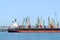 Large black red sea cargo ship while parking in the port. Port cranes download the cargo into the ship. The work of the seaport.