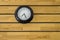 Large black round clock with arrows close-up on a yellow wooden plank wall. horizontal lines. natural texture surface