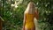 Large blonde woman in a yellow swimsuit, lingerie bodysuit stands back in an exotic forest