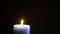 A large blue candle burns in complete darkness.