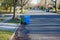 Large blue and green trash cans with wheels on a residential tree lined street waiting for trash pickup