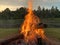 A large bonfire in the meadow next to the pond on a quiet summer evening.