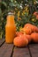 A large bottle of pumpkin juice and a fresh crop of pumpkins on a wooden table.