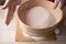 Large bowl, cutting board, sieve for sifting flour on the table. Female hands sifting flour in the home kitchen