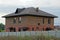 A large brick brown house with windows behind a gray concrete fence in green grass