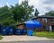 Large brown wooden house is seen with blue tarp over garage roof and two dumpsters in the driveway