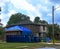 Large brown wooden house is seen with blue tarp over garage roof and two dumpsters in the driveway