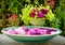 A large bvowl of crockery filled with water and many swimming leafs of pink flowers on a wooden table in front of a beautiful flow