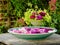 A large bvowl of crockery filled with water and many swimming leafs of pink flowers on a wooden table in front of a beautiful flow