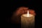 A large candle burns in the dark. On a wooden background.