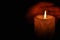 A large candle burns in the dark. On a wooden background.