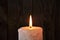 A large candle burns in the darkness on a wooden texture background