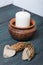 A large candle in a clay vessel. Decorated with cones and hearts cut out of paper. It stands on painted boards painted in black