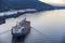 Large cargo ship sails along the river along the industrial zone leaving foamy trail