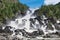 Large cascading waterfall on a summer sunny day. Big stones in forest, nature landscape