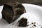 Large chopped piece of chocolate on a white ceramic plate stands on a brown wooden table