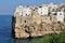 large cliff on the seashore, buildings built on the rocks right on the seashore, Polignano a Mare, people bathing in the sea