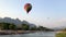 A large colorful balloon flies over the river in Laos.