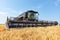 A large combine harvester against the background of a field of ripe wheat on a bright sunny day