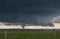 A large cone tornado under the base of a dark storm on the plains.