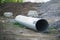 A large corrugated metal pipe with a coupler, prepared for installation, lies on a construction site next to a pile of gravel.