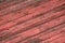 Large dilapidated dark red roof tiles with faded color texture background held together with strong red rivets