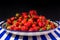 A large earthenware dish with fresh red strawberries on a blue-and-white striped table.