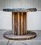 Large Empty Wooden Spool on sidewalk, and a white stripped pattern wall in the background.