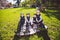 Large family Caucasian children. Three brothers and sister sitting resting on blanket outside the park. Green lawn grass