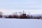 Large farming property with grain elevators and other buildings behind mixed trees