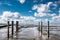 Large field of muddy brown water with wooden poles under a bright blue sky