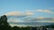 Large fluffy white clouds float on blue sky above small tropical city house roofs