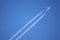 Large four engine passenger supersonic aircraft flying from left to right high in blue cloudless sky leaving long white trail