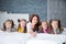 Large friendly family, many children: mom and four pretty cheerful girls triple twins sisters lying on a bed against a gray brick