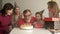 Large friendly multi-generation family standing together in home and watching grandfather blowing candles on birthday