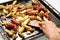 A large frying pan with fatty foods: sausages, potatoes in a rustic manner. Hand and wooden spatula