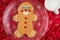 Large gingerbread cookie on a glass platter, red fabric background with gold snowflakes, white mug with milk