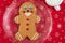 Large gingerbread cookie on a glass platter, red fabric background with gold snowflakes, white mug with milk