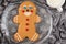 Large gingerbread cookie on a glass platter, silver fabric background with silver snowflakes, white mug with milk