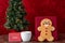 Large gingerbread cookie on a red background, Christmas tree with white lights, note to Santa, white mug with milk, wood table
