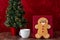 Large gingerbread cookie on a red background, Christmas tree with white lights, white mug with milk, on a wood table