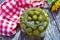 Large glass jar of green pitted olives on tabletop with checked cloth