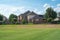 Large grassy and rolling lawn of suburban park next to upscale residential neighborhood row of two-story houses in Flower Mound,